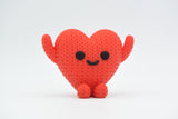 Gros plan d'une petite figurine de cœur rouge tricoté à texture crochetée et visage simple
