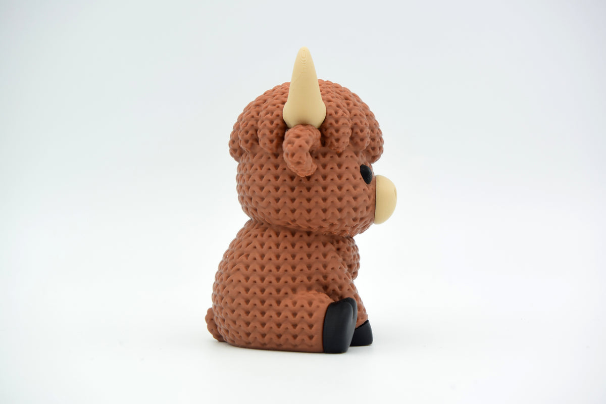 Figurine de vache Highland tricotée sur une étagère en bois avec des plantes et une déco scandinave neutre