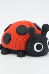 Gros plan d'une coccinelle tricotée rouge et noire, aspect crocheté, sur surface blanche