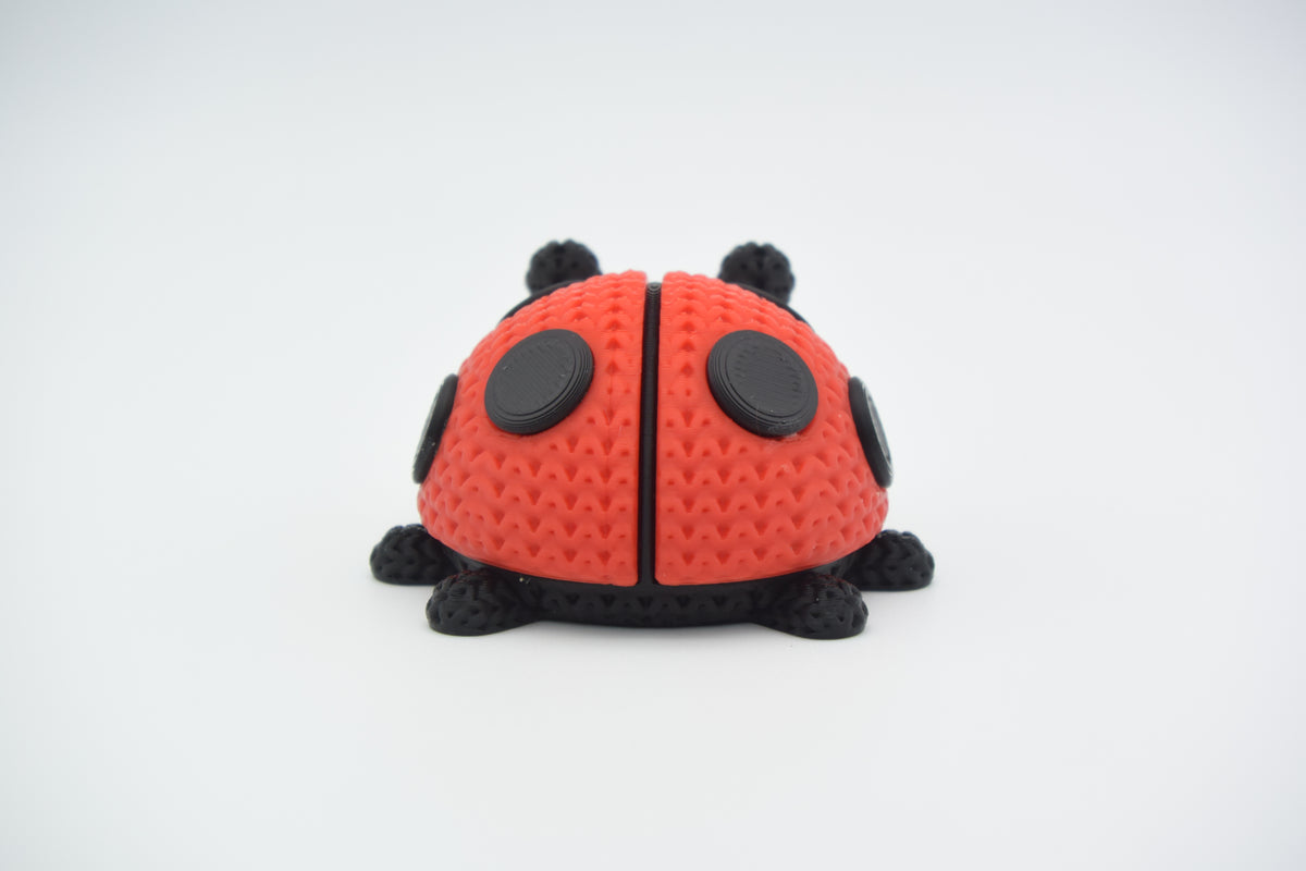 Gros plan d'une coccinelle tricotée rouge et noire, aspect crocheté, sur surface blanche