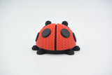 Gros plan d'une coccinelle tricotée rouge et noire, aspect crocheté, sur surface blanche
