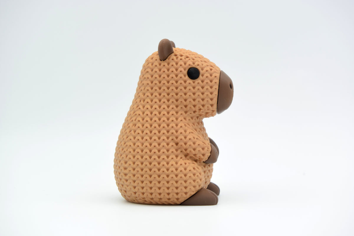 Petite figurine capybara façon tricot sur une étagère en bois avec plantes et livres, décor scandinave