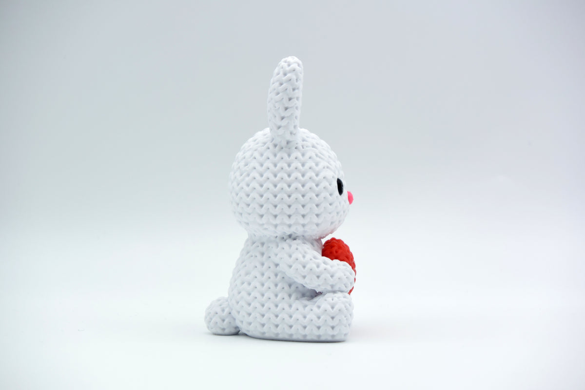 Lapin tricoté avec cœur sur une étagère en bois avec fleurs de printemps et déco de Pâques
