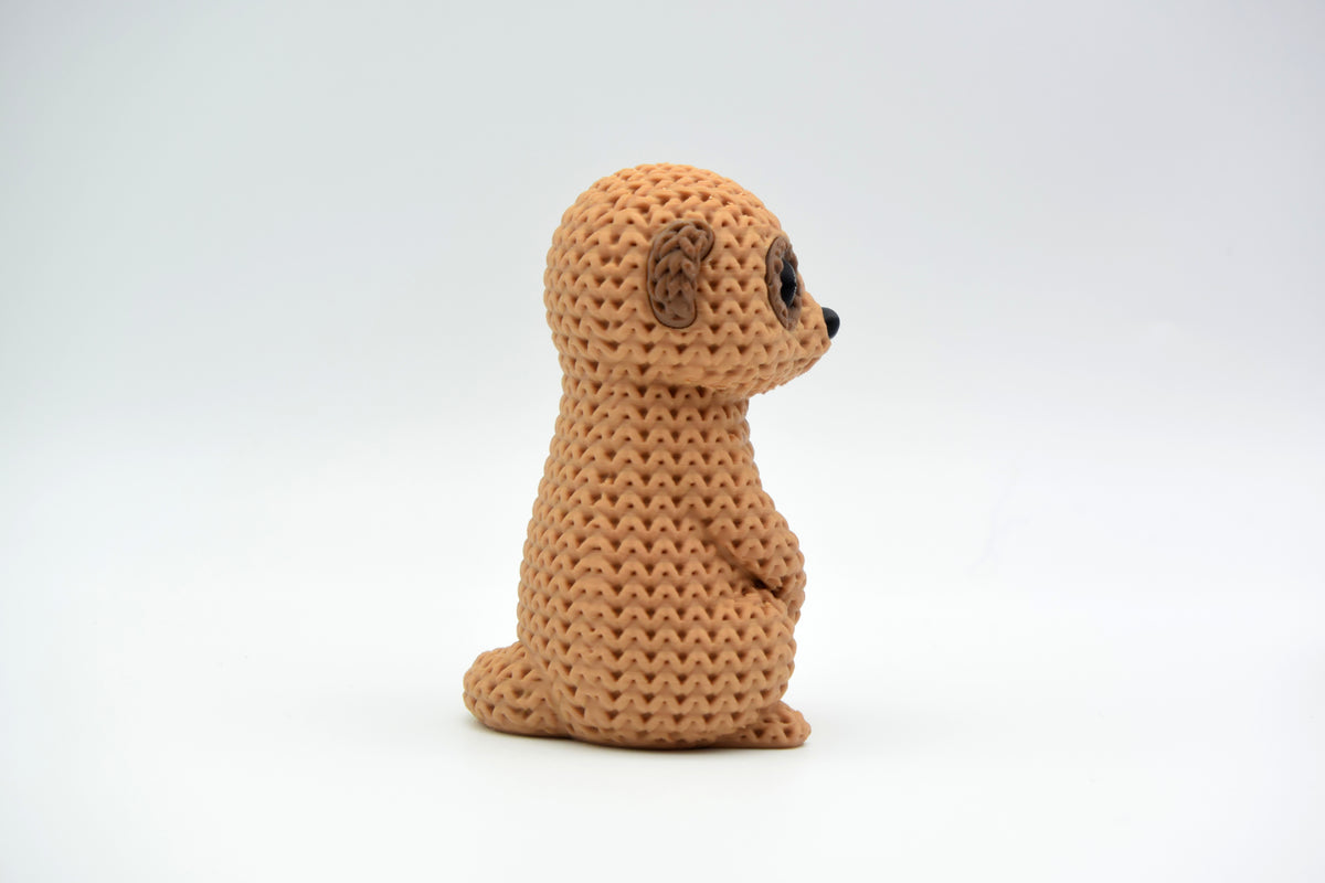 Figurine de suricate tricotée sur une étagère en bois à côté d'une petite plante et d'une déco neutre