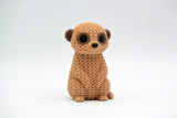 Gros plan d'une figurine de suricate tricoté à texture crochetée, debout sur fond blanc