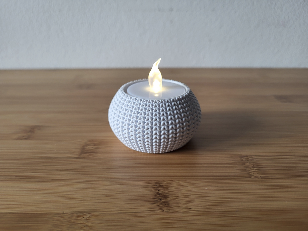 Photophore tricoté avec une bougie chauffe-plat allumée sur une étagère en bois dans un intérieur cosy