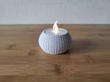 Photophore tricoté avec une bougie chauffe-plat allumée sur une étagère en bois dans un intérieur cosy