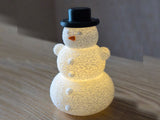 Bonhomme de neige avec chapeau et nez au-dessus d'une bougie LED